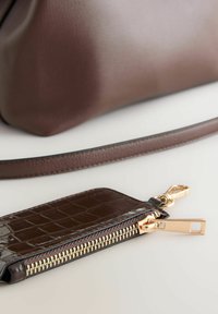 Braune Lederhandtasche mit strukturiertem Äußeren und passendem Beutel mit Krokodilprägung, goldenen Beschlägen und einem Reißverschluss.