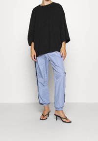 Maglietta nera oversize in cotone con scollatura rotonda, abbinata a pantaloni jogger in nylon azzurro chiaro con strisce laterali e polsini elasticizzati. Sandali neri con tacco.