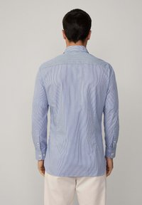 Camicia da uomo a maniche lunghe di colore azzurro chiaro con strisce verticali. Presenta polsini con bottoni e colletto a punta. Tessuto dalla texture liscia.