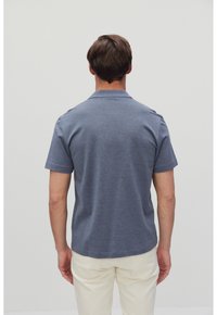 Lyhythihainen polo-paita tummansinisessä värissä, joka on valmistettu tekstuurisesta kankaasta ja jossa on kaulus sekä suora helma. Yhdistetty vaaleisiin housuihin.