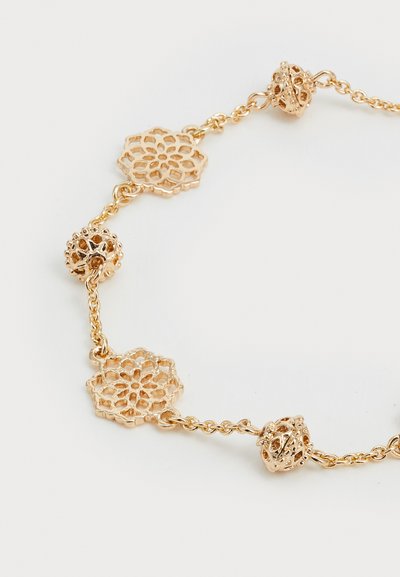 Goldfarbener Armreif mit filigranen floralen und runden spitzenähnlichen Mustern, die durch eine zarte Kette verbunden sind. Besitzt eine glatte, glänzende Textur.