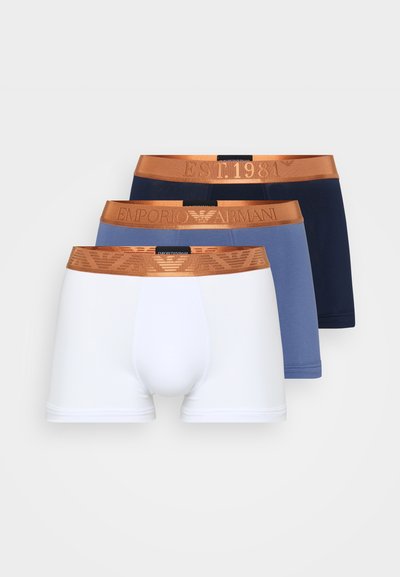 Tri pari Emporio Armani bokseric: bele, svetlo modre in temno modre. Vsak ima rjav elastični pas z blagovno znamko, na katerem piše "EST. 1981."