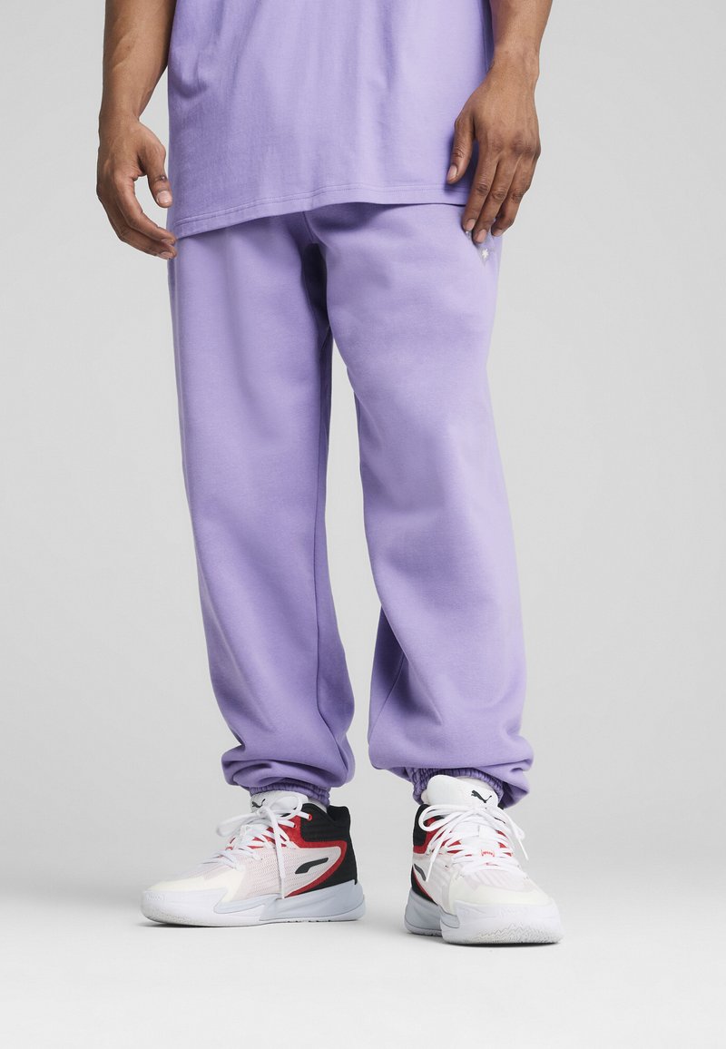 Lilla sweatpants lavet af blødt stof har en elastisk talje og manchetter. Bæres med hvide og sorte sneakers med røde detaljer.