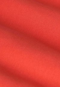 Tissu corail avec une texture lisse et douce, légèrement brillante, présentant une couleur unie sans motifs ni accents.