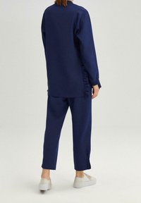 Marine lounge set met een langslueve top met zijkanten fronsen en relaxte pasvorm broeken. Zachte stof met een gladde textuur en eenvoudig ontwerp.