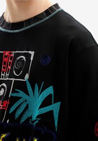 Camisa negra con bordado abstracto colorido que incluye formas de plantas azules, rectángulos rojos y blancos, y patrones circulares en el área del pecho.