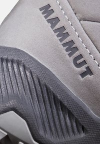 Szare buty outdoorowe z teksturowaną cholewką z zamszu, widocznym logo „MAMMUT” oraz gumową podeszwą z wyraźnymi rowkami i wzorami.