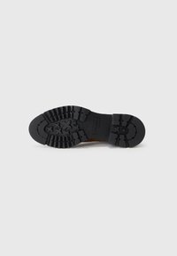 Black rubber sole with deep treads, textured surface, and detailed patterns. Brown leather upper with clean lines and stitching visible.