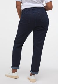 Tumši zili džinsu bikses ar sašaurinātu piegriezumu, ar sarullētiem galiem un divām aizmugurējām kabatām, kurām ir niansēta izšuvuma dizains.