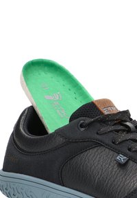 Zapato de cuero negro con un acabado texturizado, que cuenta con una suela de color gris claro. Plantilla verde visible en el interior, etiquetada con la marca y el tamaño.