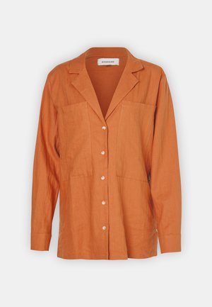 Sötét narancssárga lenvászon ing, amit kivágott gallér, két melltáska és hat elülső gomb díszít. Hosszú ujjak, csuklópánttal.