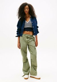 Denimjack, cropped gestreept top, olijfgroene cargobroek, witte sneakers met bruine zolen, voorzien van zakken en een losse pasvorm.