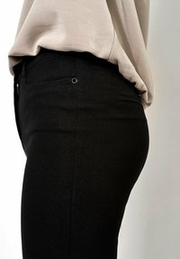Zwarte slimfit broek heeft een strakke snit, met een gladde textuur, kleine zijzakken en minimale hardware. Gecombineerd met een lichtbeige top.