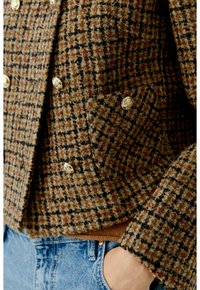Bruine en zwarte geruite wollen blazer met gouden knopen, gedragen over een bruine top en gecombineerd met blauwe denim jeans.