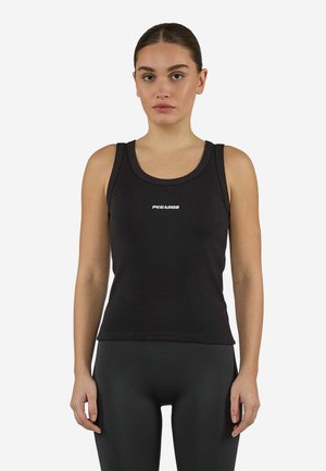 Kvinde iført sort ærmeløs top med ordet "PEGADOR" på brystet og sorte leggings, stående med armene afslappet langs siden.
