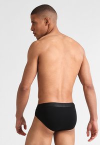 Slip neri da uomo con una texture liscia e un elastico in vita, caratterizzati da un design minimalista. La vista posteriore mostra una vestibilità aderente.