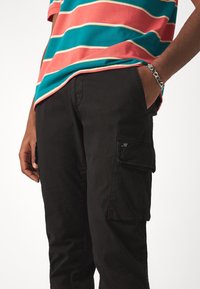 Černé cargo kalhoty s úzkým střihem, vybavené bočními kapsami, jemným logem a hladkou, odolnou strukturou látky.