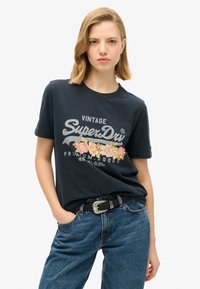 T-shirt in cotone blu navy con un design floreale ricamato in rosa e giallo, stampa "SuperDry" in argento e colletto girocollo classico.