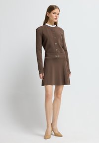 Bruine gebreide jurk met een ronde halslijn, knopen aan de voorkant en een getailleerde taille. Heeft een uitlopende rok en een metallic accentdetail.