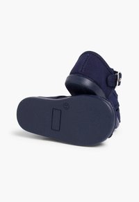 Navy blue fabric shoe with a back strap, textured sole, and a simple buckle detail. Features a flat rubber sole for stability.