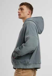 Grey, hooded sweatshirt with a relaxed fit, ribbed cuffs and hem, drawstring hood, and subtle stitching detail, made from soft fabric.