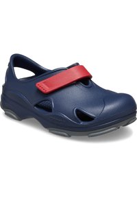 Zoccoli blu navy con una fascetta rossa in velcro, dotati di fori di ventilazione, superficie testurizzata e suola in gomma grigia per un'ottima aderenza.