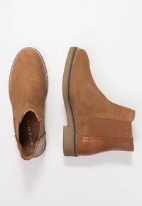 Bottines Chelsea en suède et cuir marron avec panneaux latéraux élastiques et semelles en caoutchouc texturé sur fond blanc.