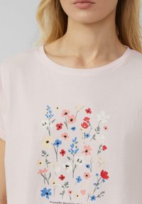 T-shirt rose clair à manches courtes avec un imprimé floral coloré comprenant des fleurs rouges, bleues, jaunes et roses sur le tissu.