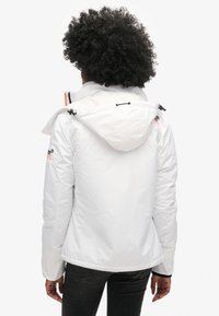 Biała ocieplana kurtka z kapturem, z regulowanymi paskami, bocznymi kieszeniami i elastycznymi mankietami. Gładka tekstura z lekko błyszczącym wykończeniem.