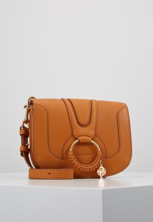 Sac bandoulière en cuir marron clair avec anneau doré et détail tressé, bandoulière réglable, logo "See By Chloé" embossé à l’avant.