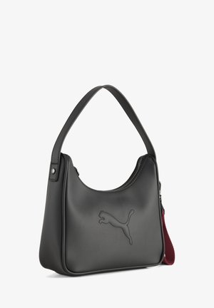 Zwarte leren schoudertas met een gebogen ritssluiting aan de bovenkant, een geperst puma-logo aan de voorkant en een rood stoffen bandje aan de zijkant bevestigd.