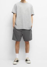 T-shirt gris en coton, manches courtes, encolure arrondie, assorti à un short gris foncé avec une ceinture élastique et des poches latérales. Baskets beiges.