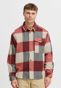Red, gray, and beige plaid flannel shirt with a button-up front and a chest pocket. Features a collared neck and long sleeves.