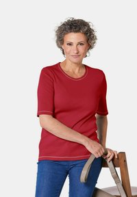 Rotes geripptes T-Shirt mit kurzen Ärmeln und rundem Halsausschnitt, kontrastierendem hellen Nähten, kombiniert mit blauen Jeans und einem grauen Gürtel in der Hand.