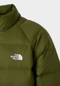 Jachetă puffer de culoare verde măslinie cu guler înalt, având un logo brodat alb pe piept și un design matlasat pentru izolație.
