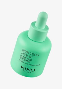 Zielona butelka z zakraplaczem z matowego szkła o zaokrąglonym kształcie. Czarny napis na etykietach informuje o "SERUM TECH SKÓRY", "DODATKU OCZYSZCZAJĄCYM" oraz nazwie marki "KIKO MILANO."