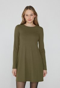 Abito lungo a maniche lunghe verde oliva a costine con scollatura rotonda, silhouette leggermente svasata e texture morbida. Non presenta decorazioni visibili.