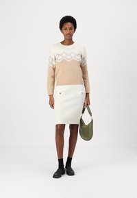 Maglione beige e crema con motivo a zigzag; gonna bianca a coste con due bottoni; borsa verde; calzini neri e mocassini.