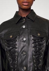 Svart läderjacka med knäppningsdesign, framträdande snörningsdetaljer på framsidan och metalldetaljer.