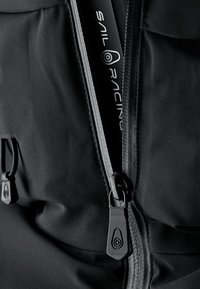 Chaqueta de navegación negra con una textura suave, que presenta un robusto cierre, detalle de logo y cierres de cordón ajustables.