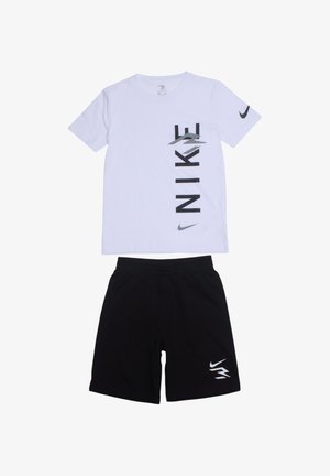 T-shirt blanc à manches courtes avec lettrage vertical noir "NIKE" et logo ; associé à un short noir avec un petit logo sur la jambe.