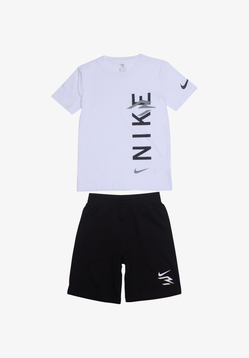 T-shirt blanc à manches courtes avec lettrage vertical noir "NIKE" et logo ; associé à un short noir avec un petit logo sur la jambe.