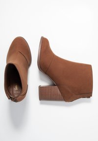 Brązowe botki do kostki wykonane z materiału przypominającego zamsz, z obcasem typu klocek o fakturowanym wzorze oraz bocznym zamkiem błyskawicznym do zamykania.