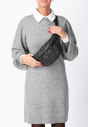 Black quilted crossbody bag with a smooth leather strap, featuring a diamond pattern and a sleek design. Worn on a gray sweater.