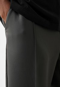 Pantalons de sport ajustés en matériau gris foncé. Dotés d'une texture lisse et de détails sur les coutures latérales. Convient pour les vêtements de sport.