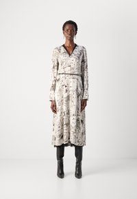 Long-sleeve, collared dress in light fabric featuring a monochrome architectural print, fitted waist with a belt, and flowing skirt.