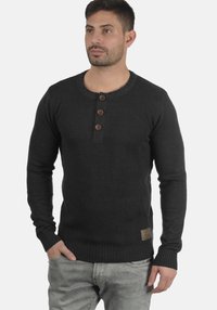 Maglione grigio scuro in maglia con scollatura rotonda, tre bottoni di legno sul davanti, polsini a coste e un'etichetta in pelle del marchio sull'orlo.