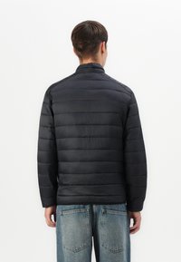 Black puffer jacket with horizontal quilted pattern, high collar, and gathered cuffs, paired with light blue loose-fitting jeans.