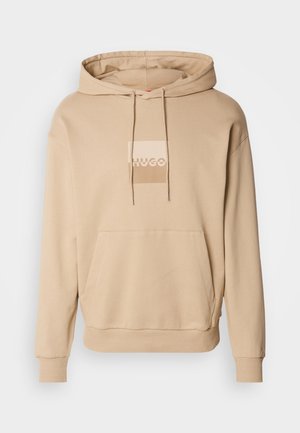 Bež kapuća sa prednjim džepom, kapuljača sa užetom i pravougaoni logo u svetlije bež boje. Napravljena od mekanog pamučnog materijala, sa rebrastim manžetama.