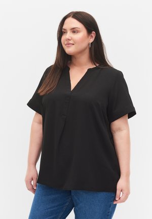 Blusa negra de manga corta con diseño de cuello en V. Fabricada en tejido suave, cuenta con un corte relajado y sutiles aberturas laterales. Combinada con jeans azules.